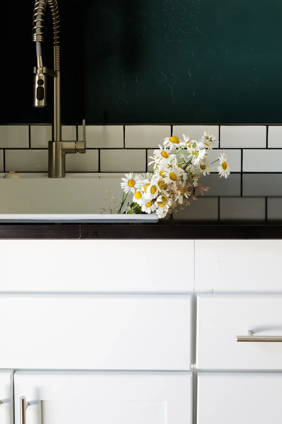 Un fregadero y un grifo de cocina están sobre armarios blancos, con flores en la encimera.
