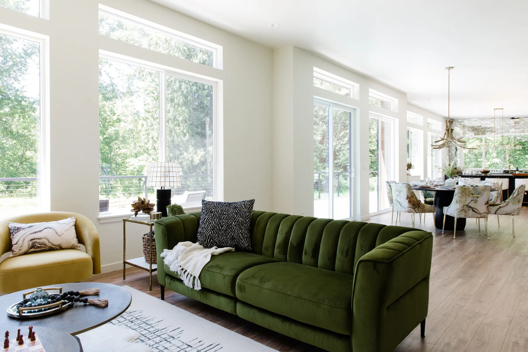 Una luminosa sala de estar y comedor con un sofá verde junto a grandes ventanas.