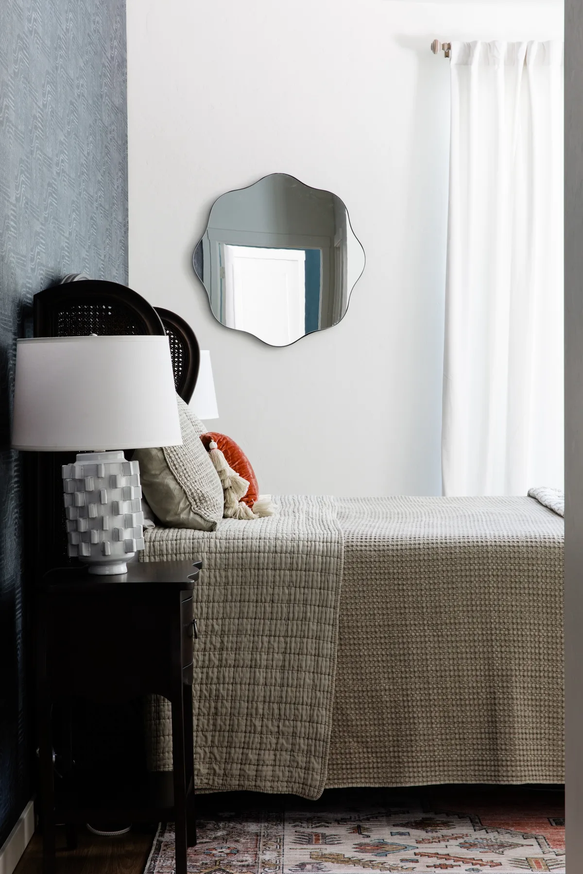 Un dormitorio con una cama tendida junto a una ventana con cortinas blancas.