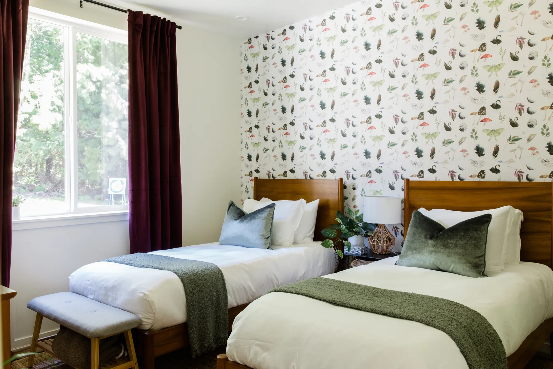 Un dormitorio con dos camas, ropa de cama verde y papel tapiz botánico.
