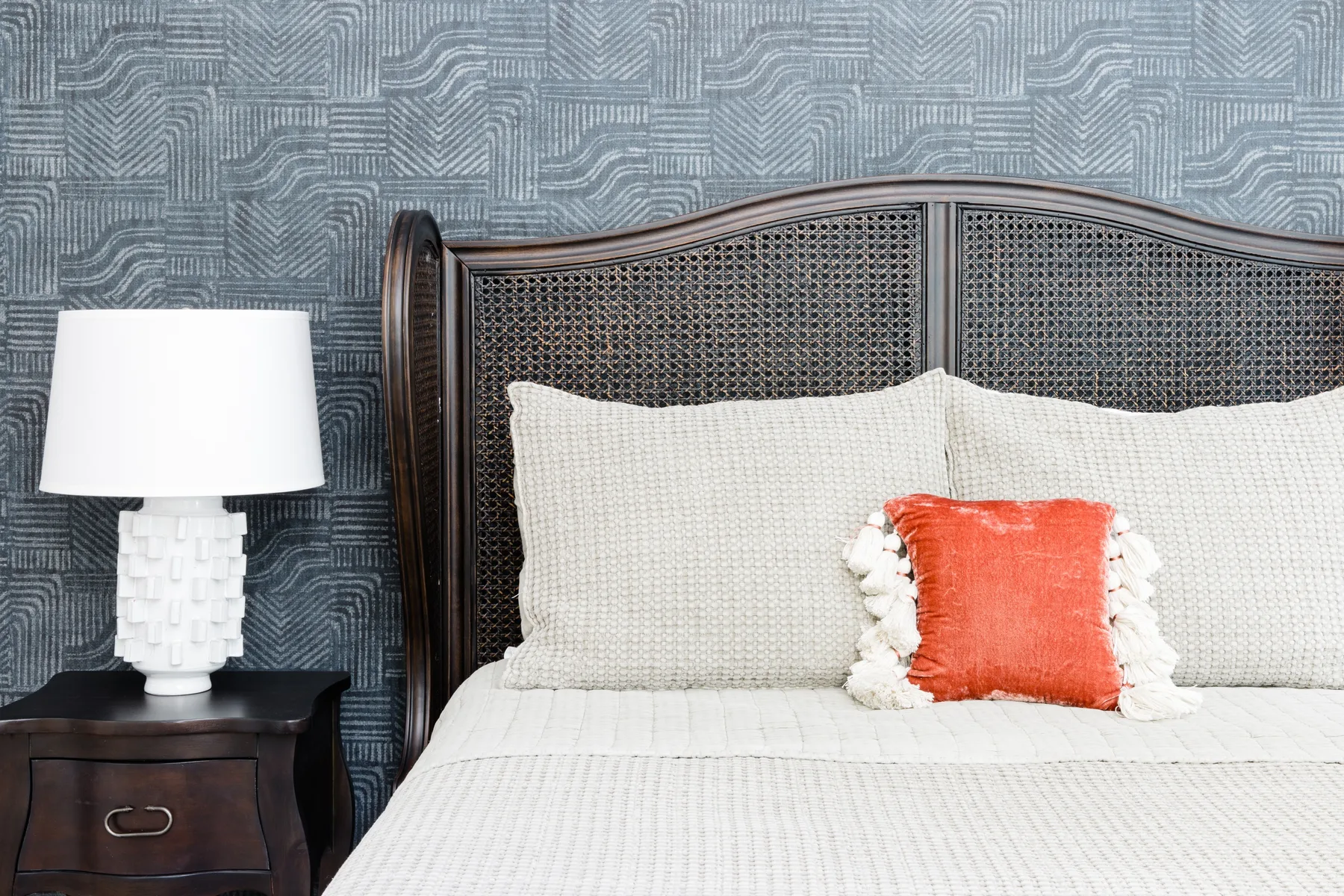 Un dormitorio con una cama frente a una pared azul estampada y un cojín naranja.