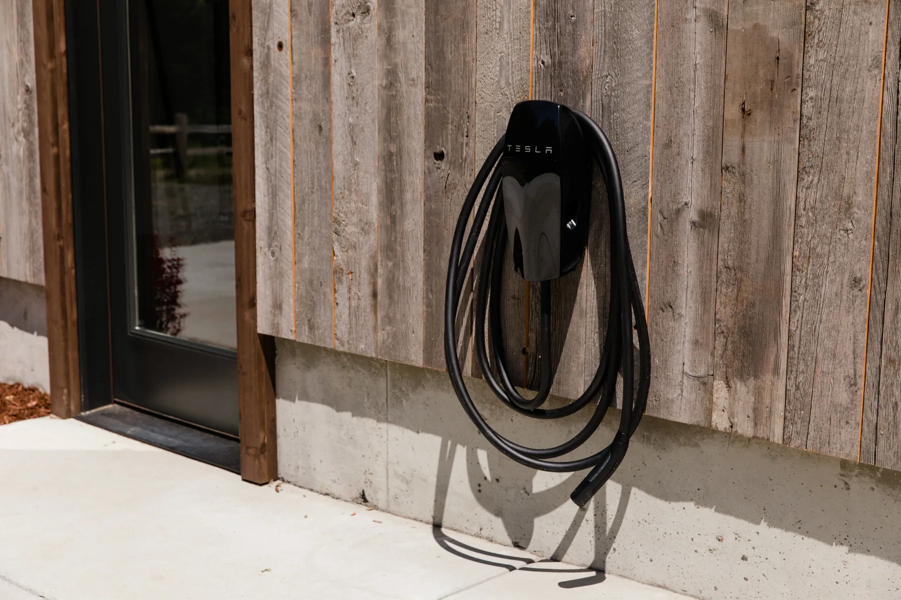 Un cargador de vehículo eléctrico está montado en un revestimiento de madera junto a una puerta de vidrio.