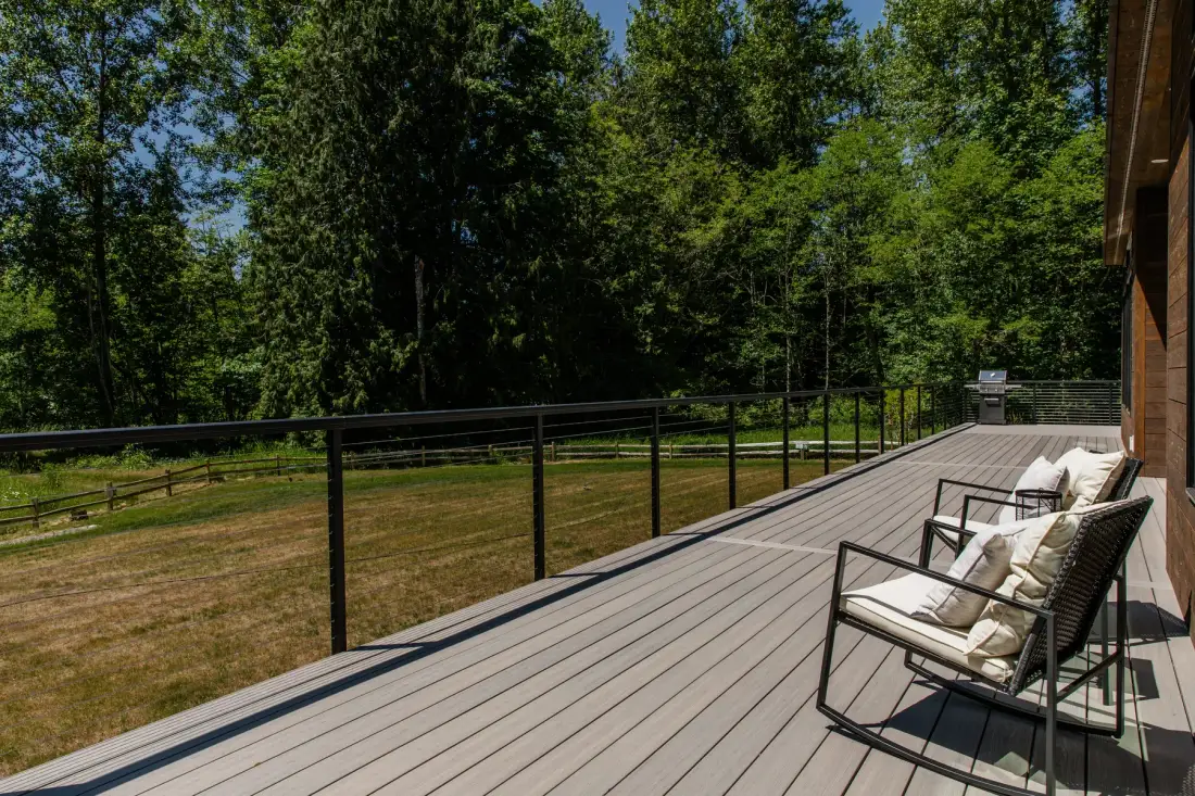 Una terraza de madera con asientos al aire libre da a una zona de césped y árboles.