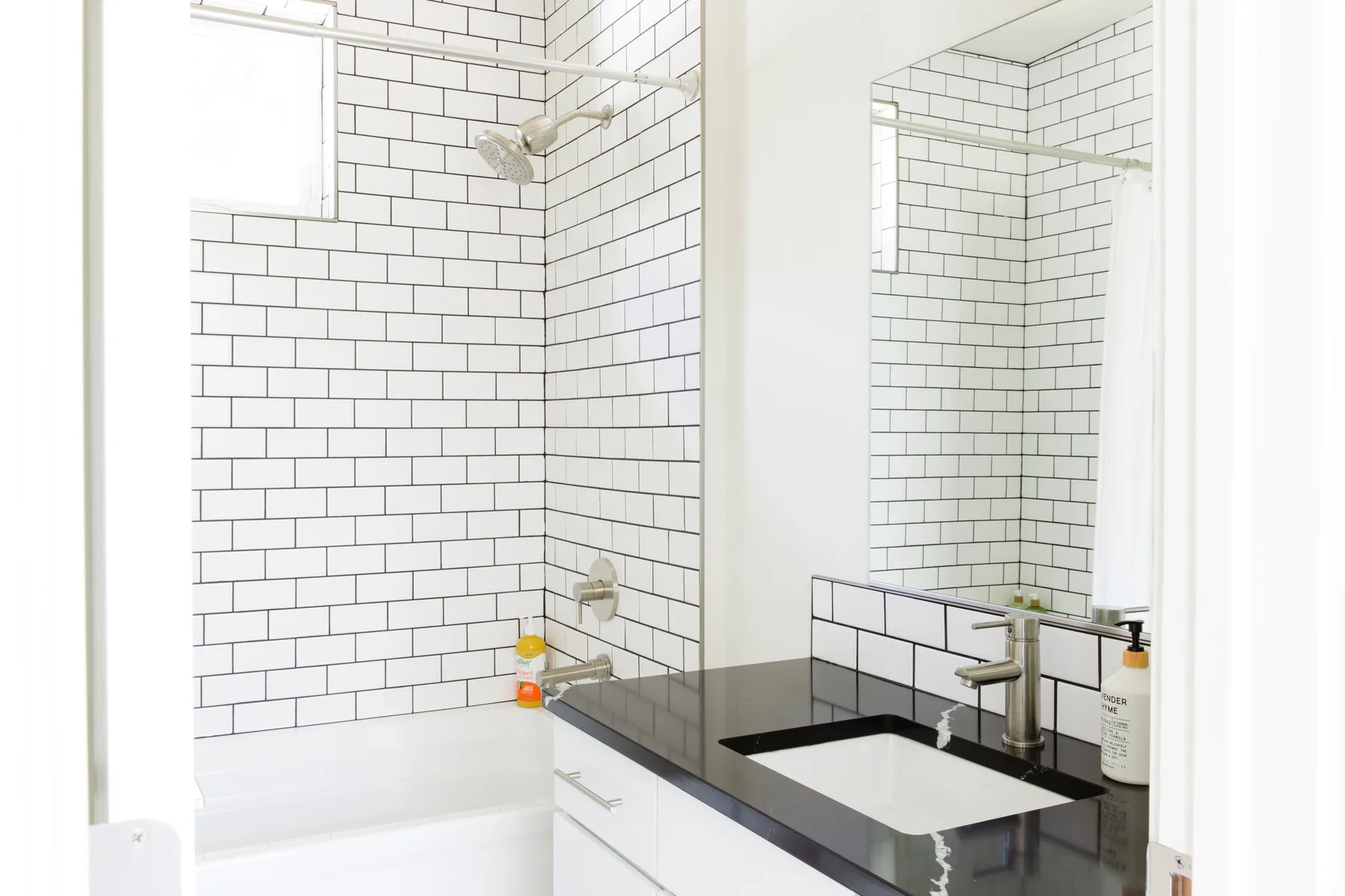 Un baño luminoso con una ducha de azulejos y un lavabo bajo un espejo.