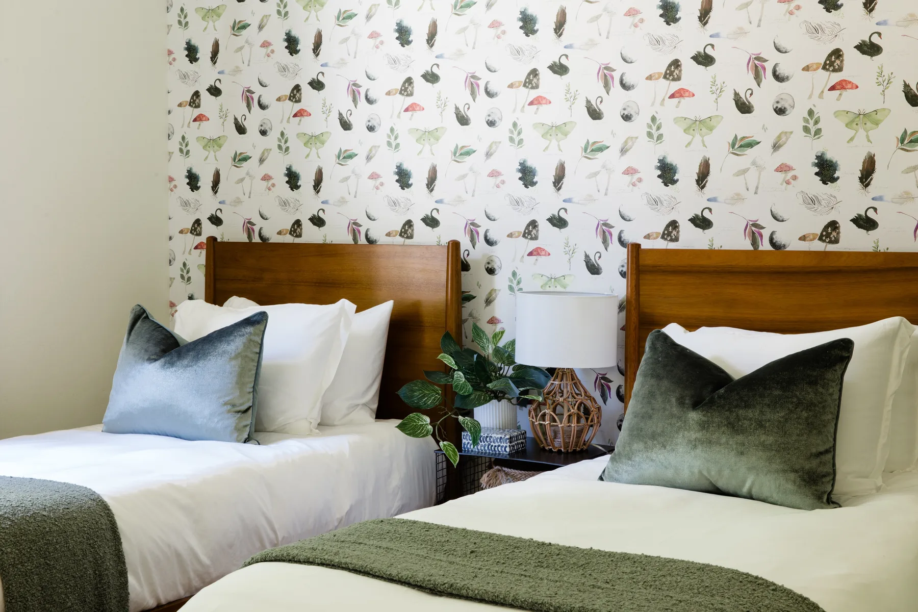 Un dormitorio con dos camas, papel tapiz estampado y una lámpara de noche.