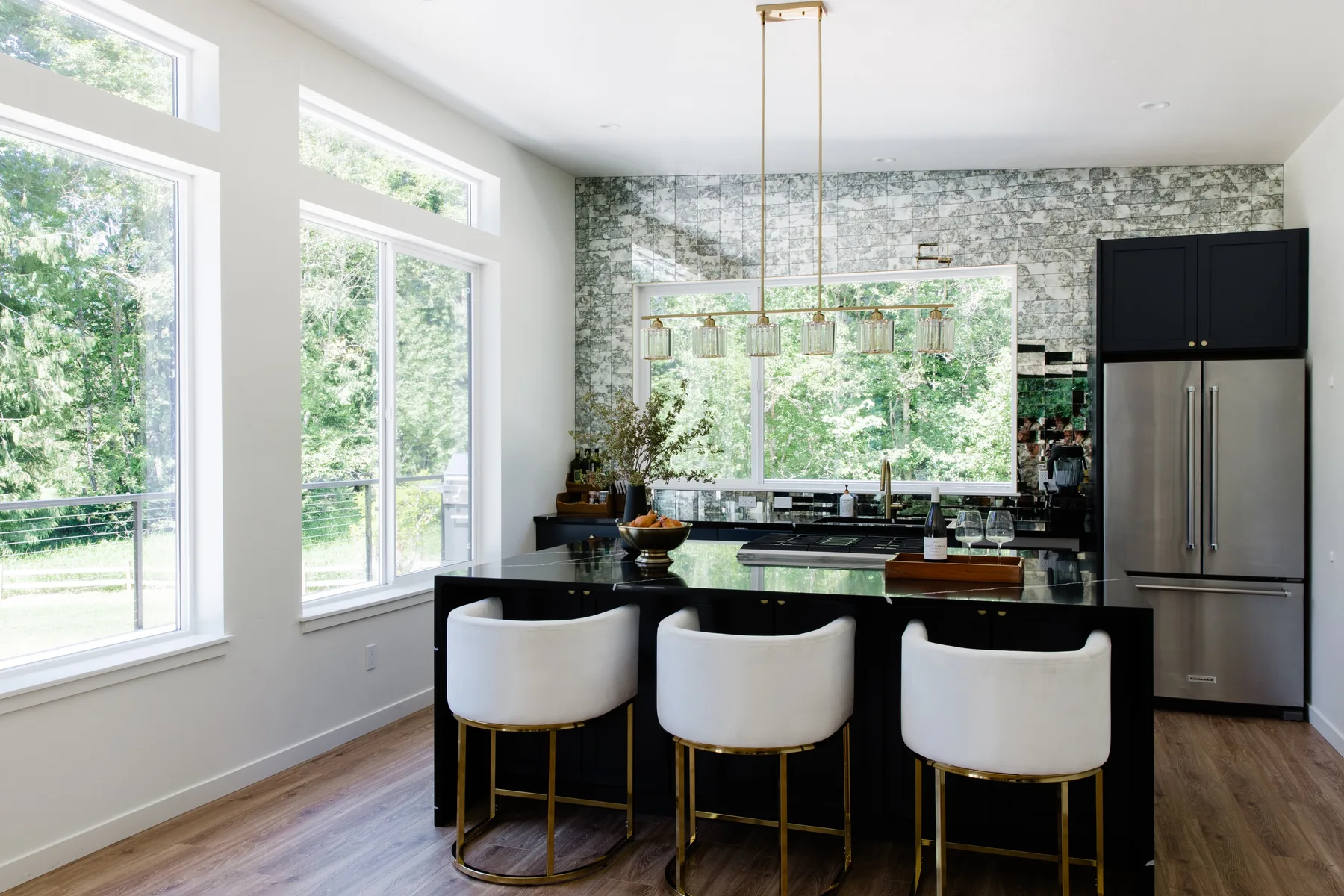 Una cocina moderna y luminosa con una isla oscura, asientos blancos y ventanales.