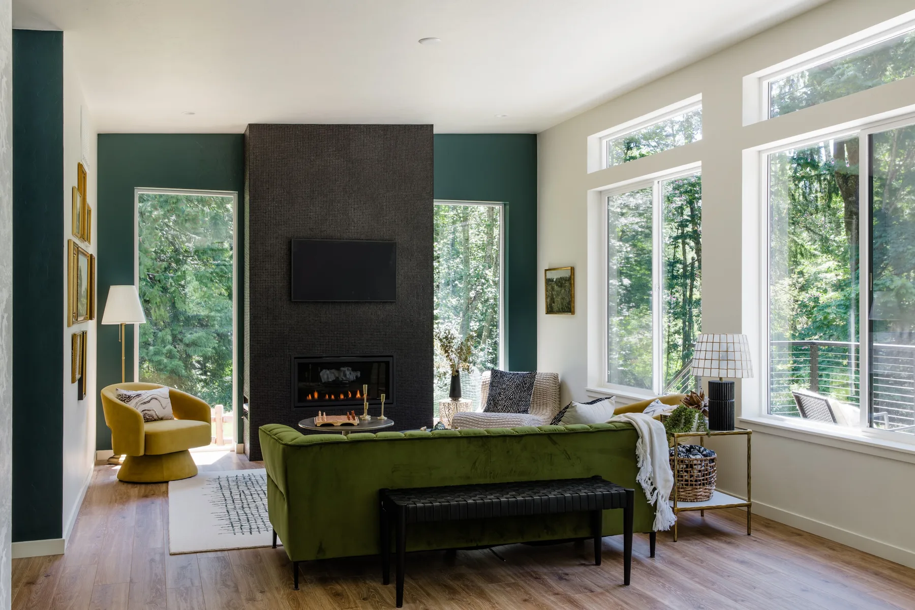 Una sala de estar con asientos verdes frente a una chimenea y ventanas grandes.