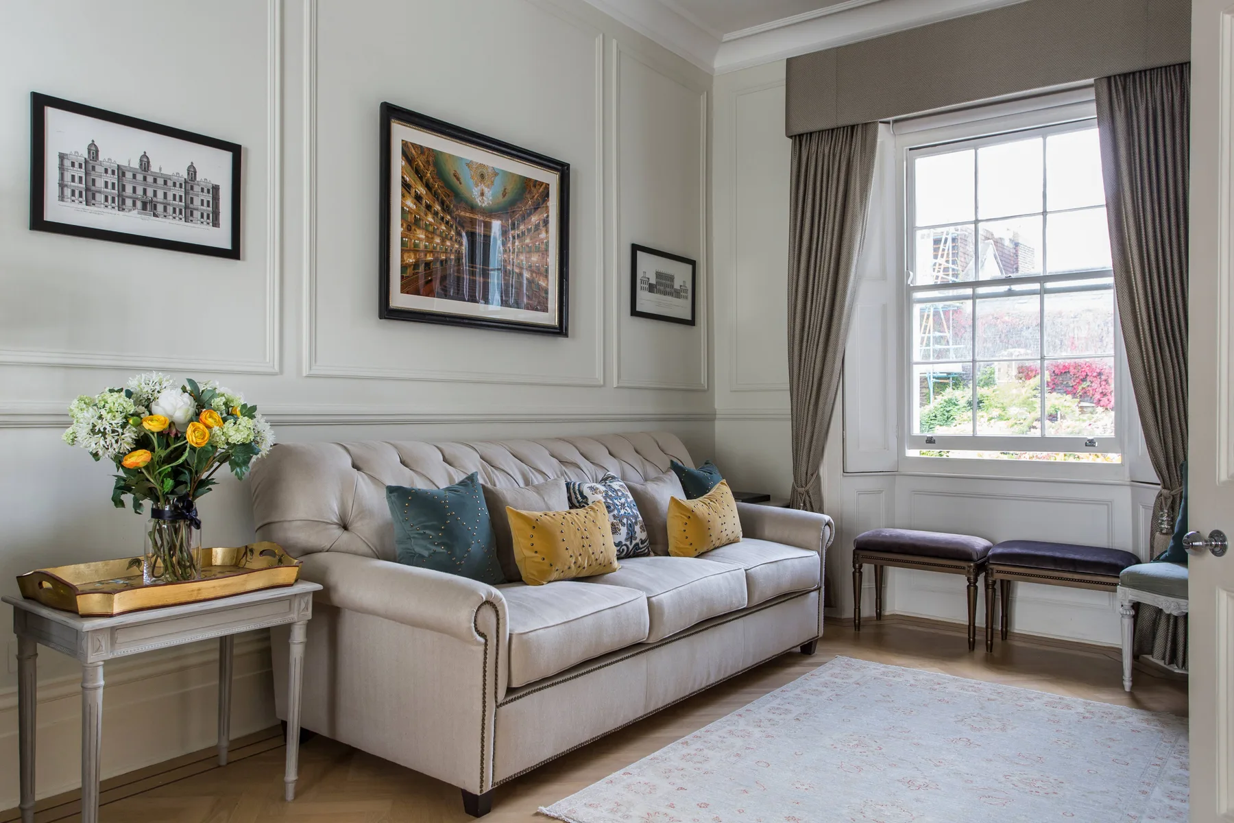 A bright living room with a sofa, framed artwork, and a large window.