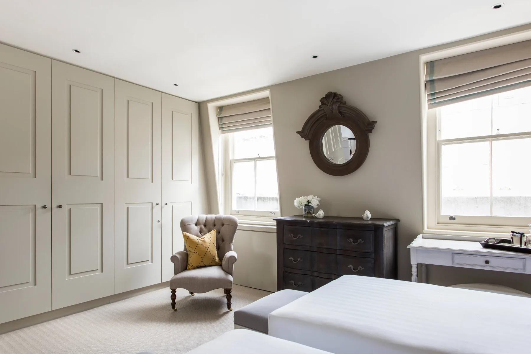 A bright bedroom with a bed, built-in wardrobes, and a dresser.