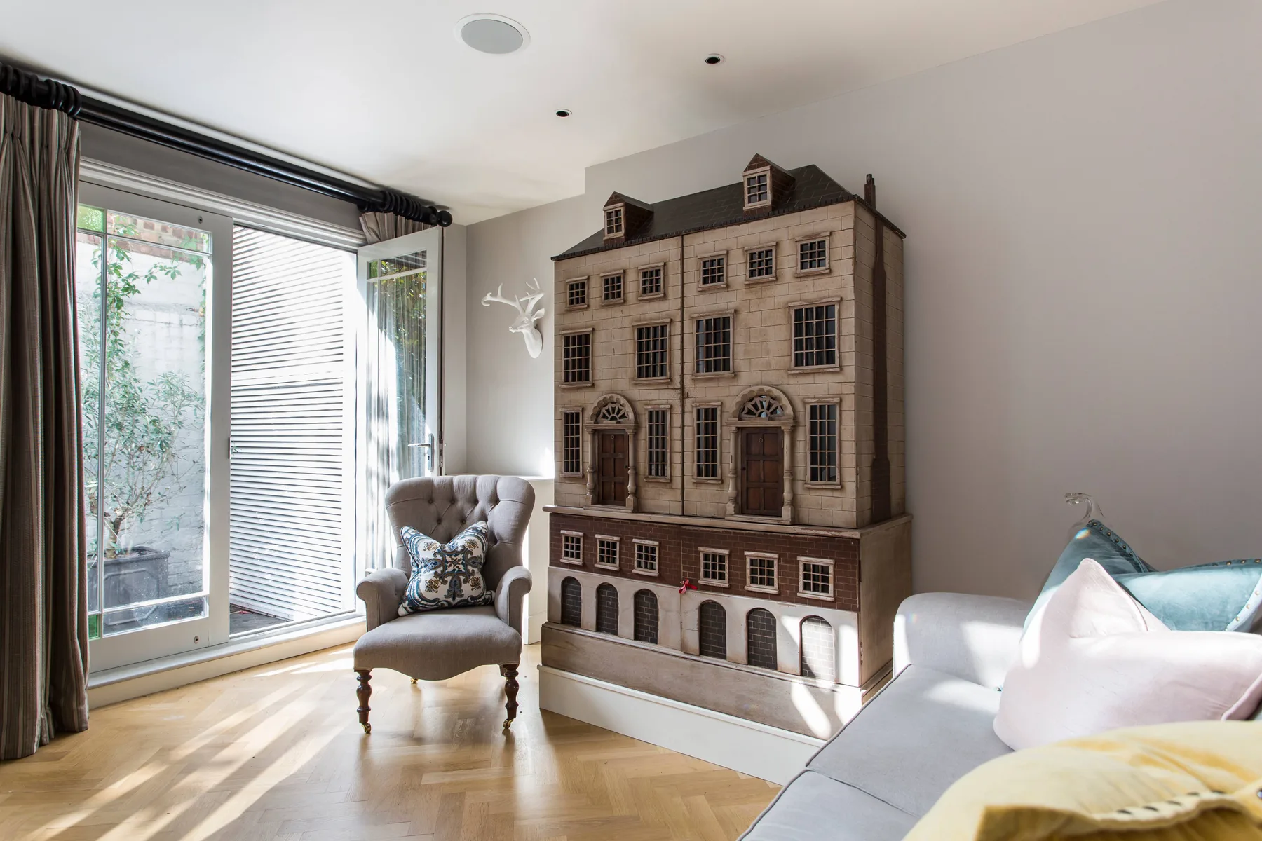 A bright living room with a large decorative dollhouse beside the seating.