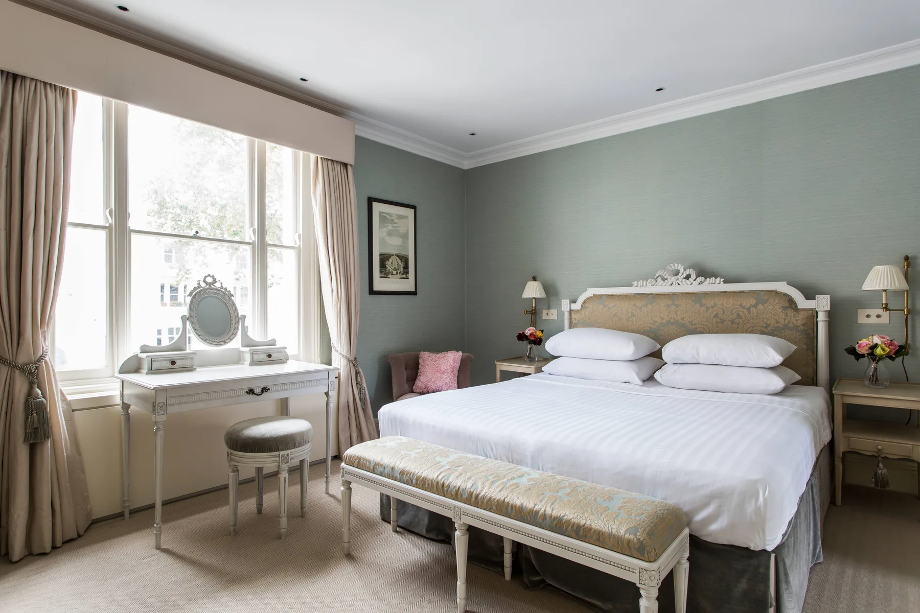 A bedroom with a large bed, a window, and a dressing table.