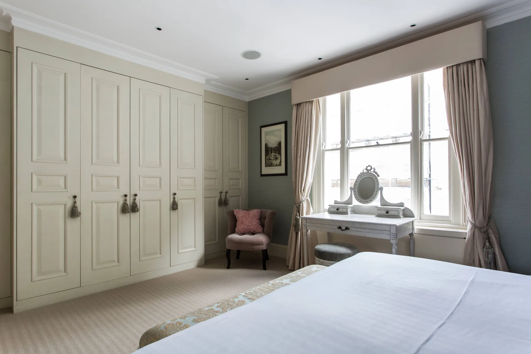 A bedroom with a bed, fitted wardrobes, and a vanity beside the window.