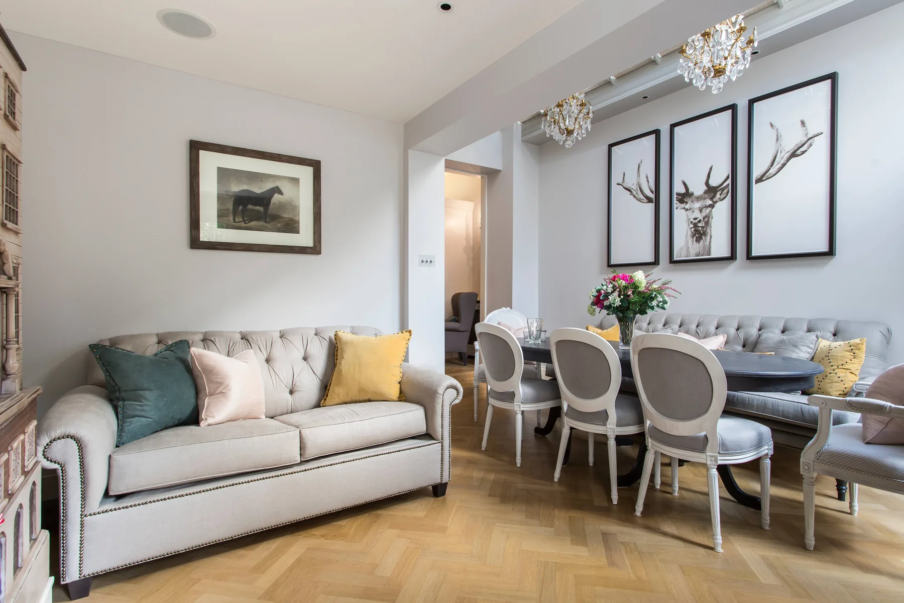 A bright living and dining room with upholstered seating, a table, and framed artwork.