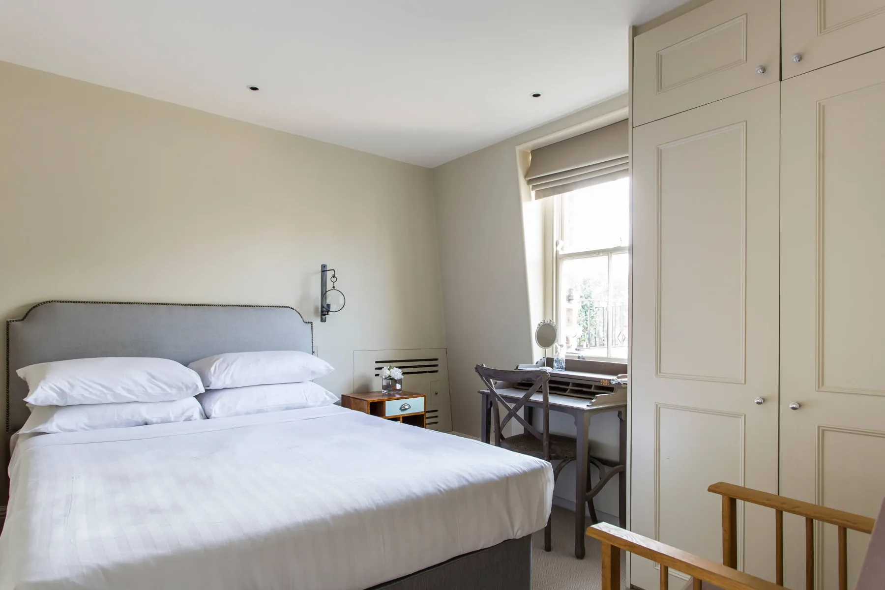 A bedroom with a bed, a desk by the window, and built-in cabinets.