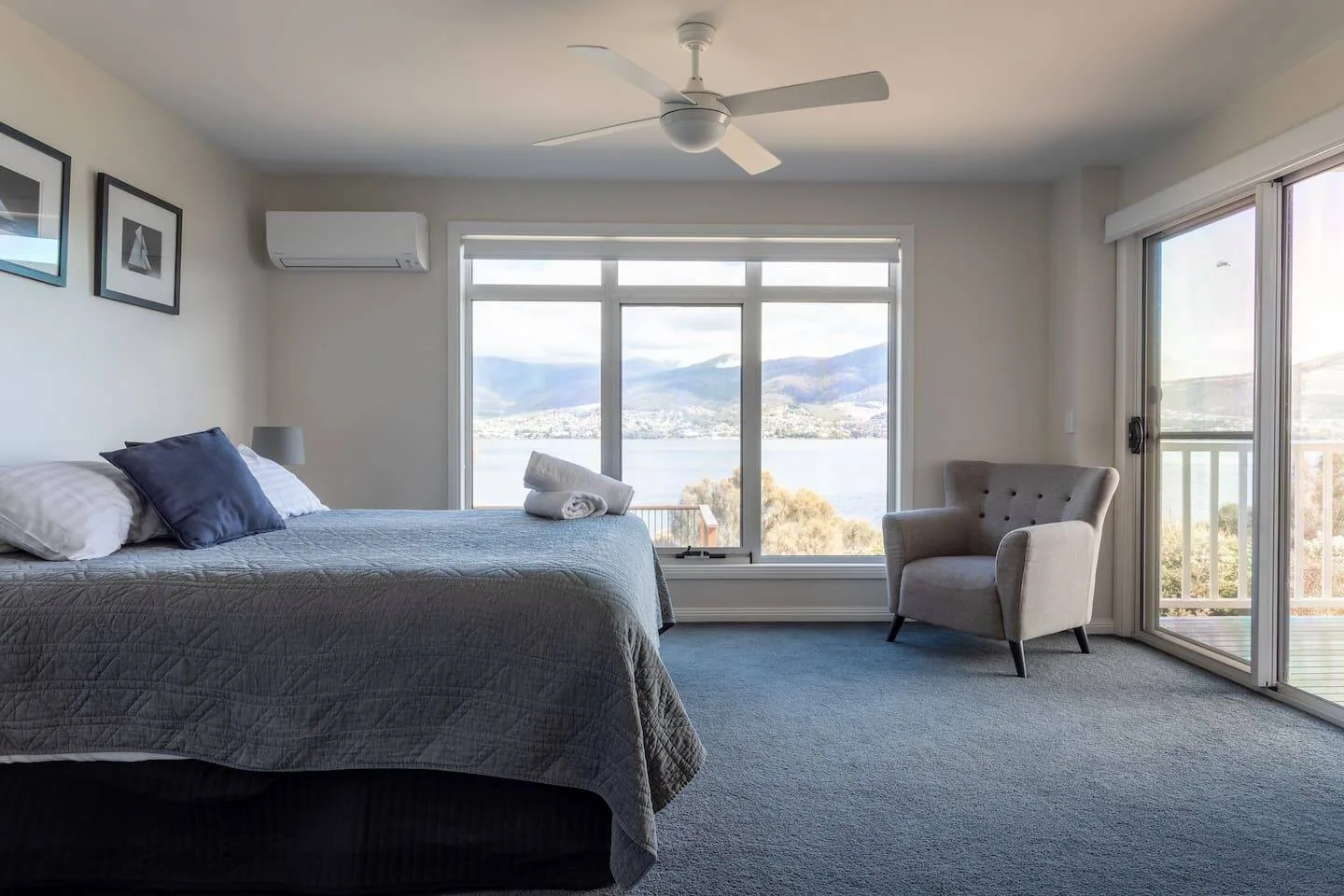 A bedroom with a bed, ceiling fan, and windows overlooking the water.