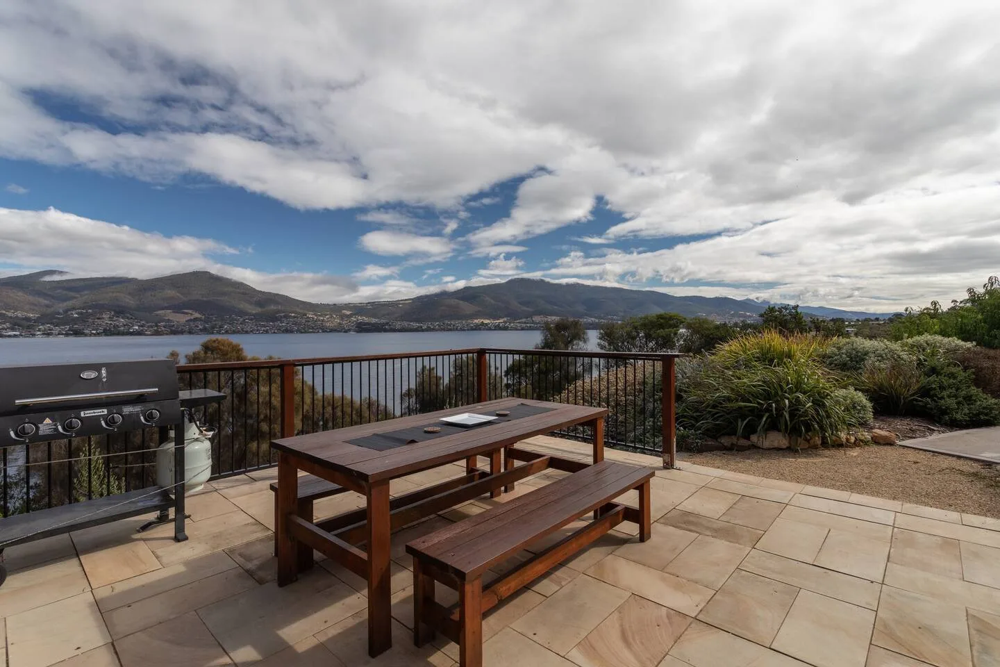 A paved patio has a picnic table and barbecue beside a body of water.