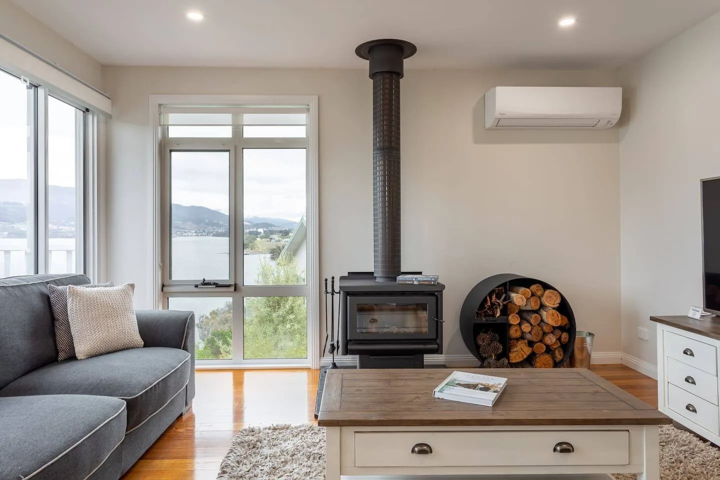 A bright living room with a wood-burning stove and large windows overlooking the water.