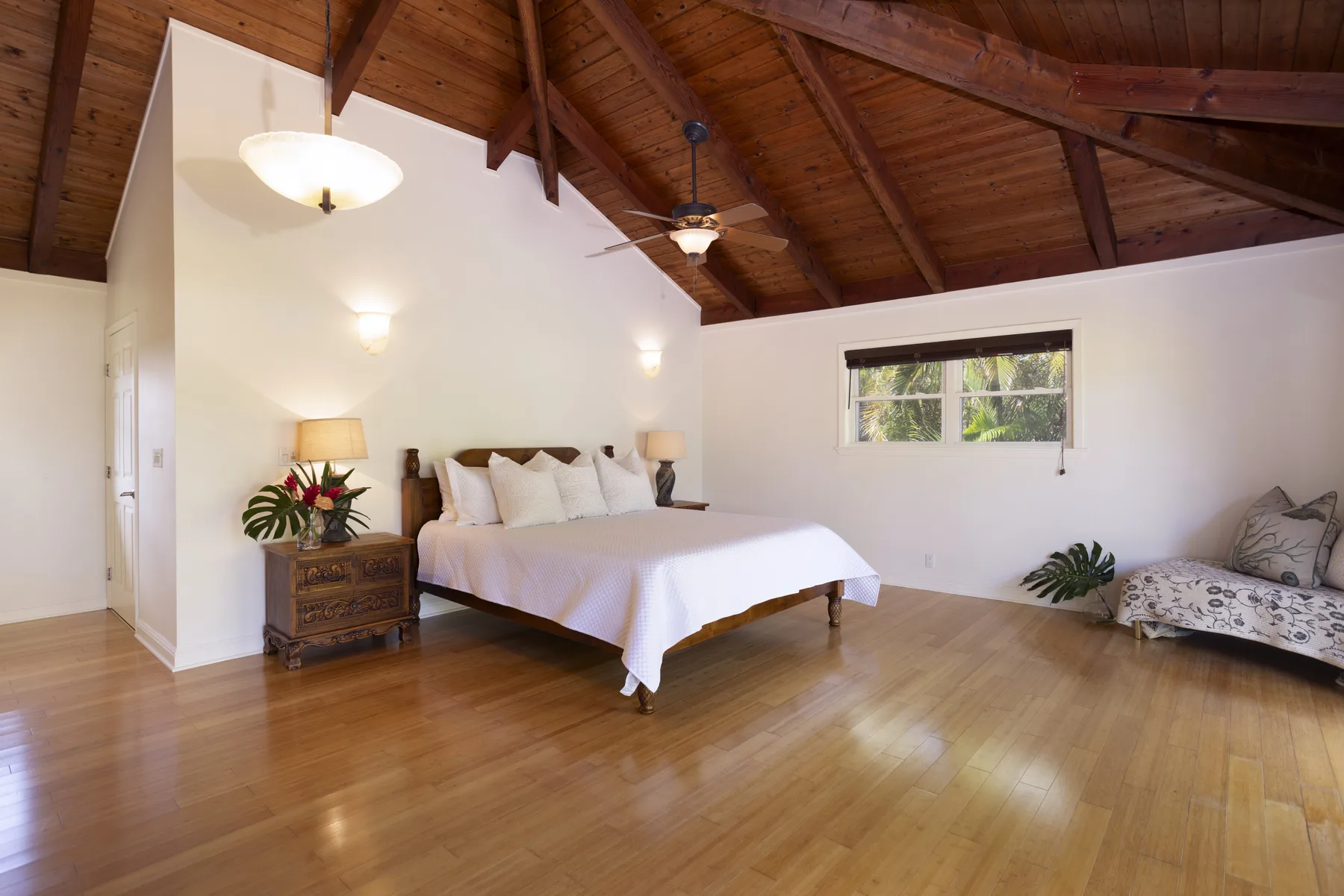 A bright bedroom with a bed, a wooden ceiling, and a small seating area.