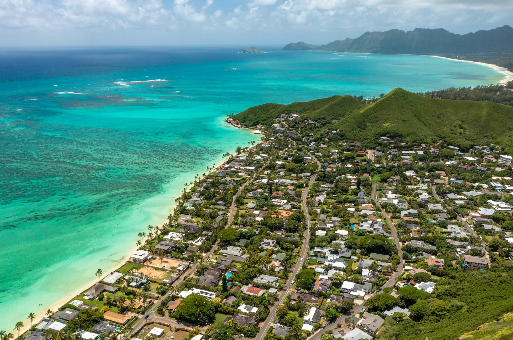 Aerial view of a coastal neighborhood beside turquoise water and a sandy beach.