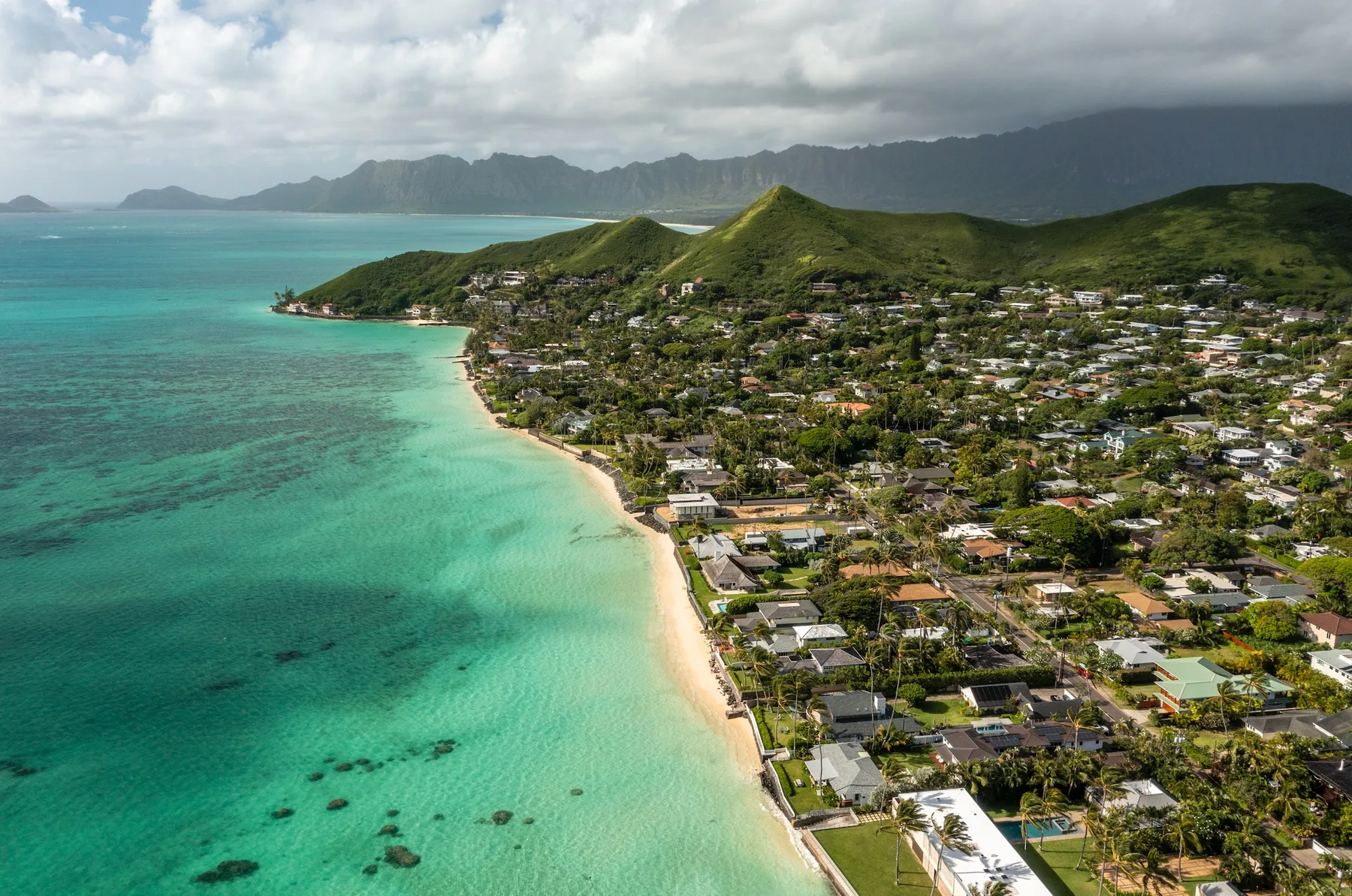 Aerial view of a coastal town along a turquoise bay and green hills.