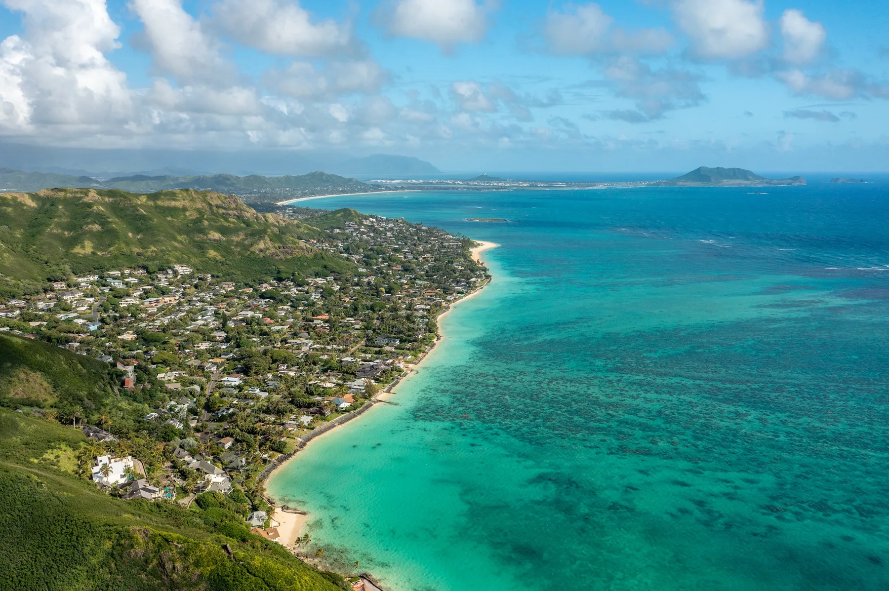 An aerial view shows a coastal town along a curving turquoise shoreline.