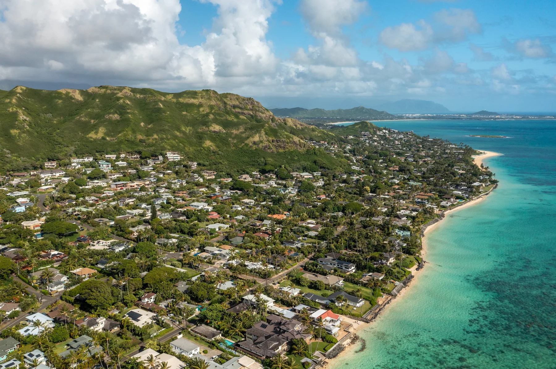 Aerial view of a coastal neighborhood beside turquoise water and a green hillside.