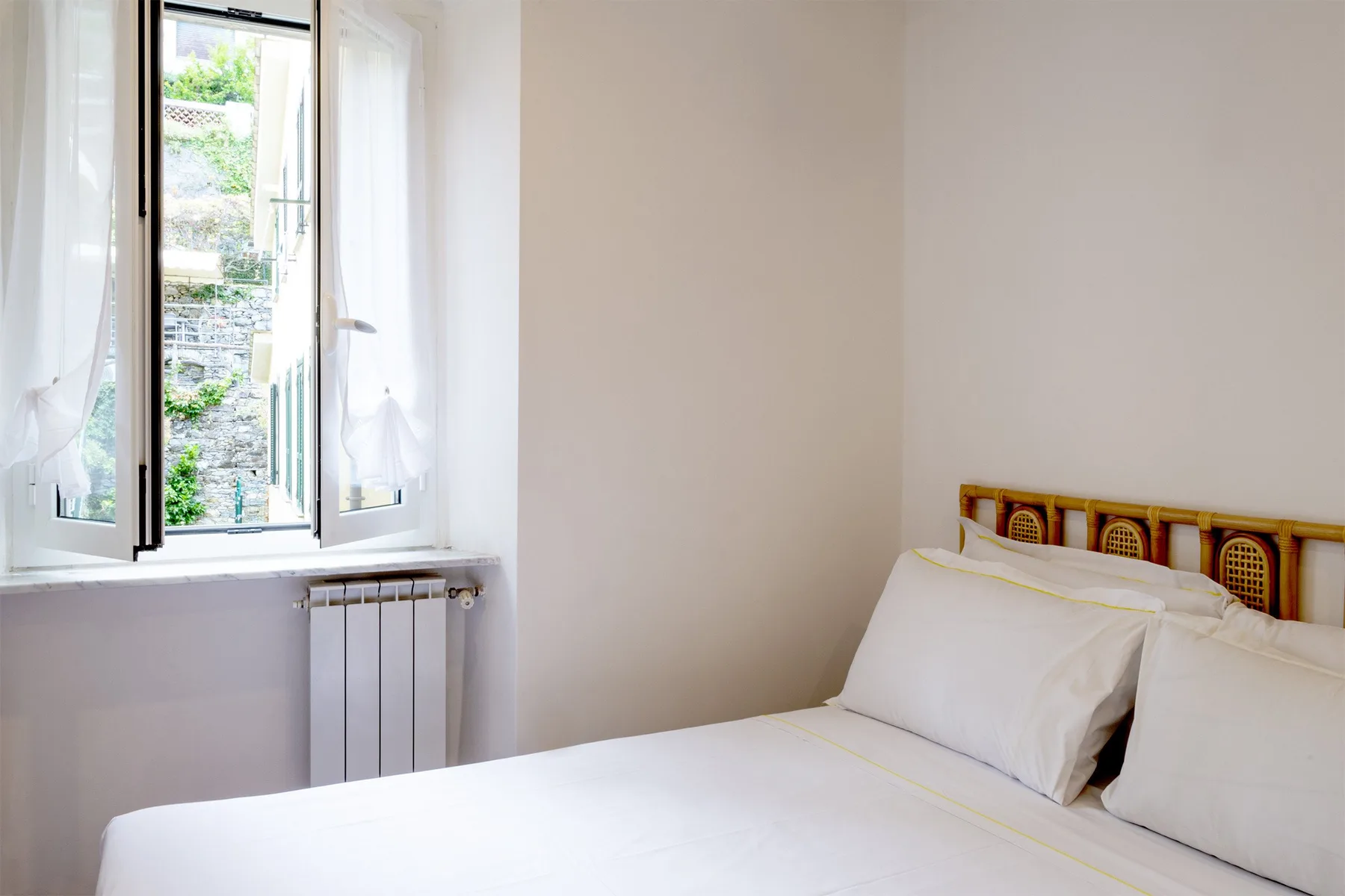 Un dormitorio luminoso con ropa de cama blanca y una ventana con vistas a la vegetación.