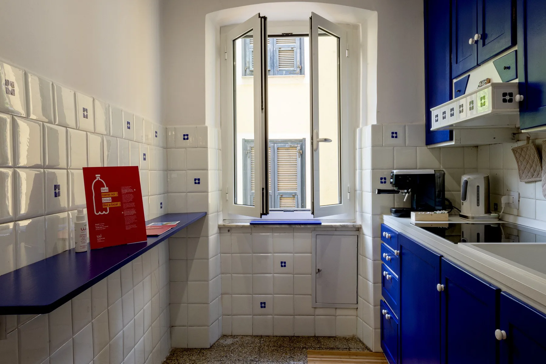 Una cocina con azulejos, armarios azules y una ventana abierta.