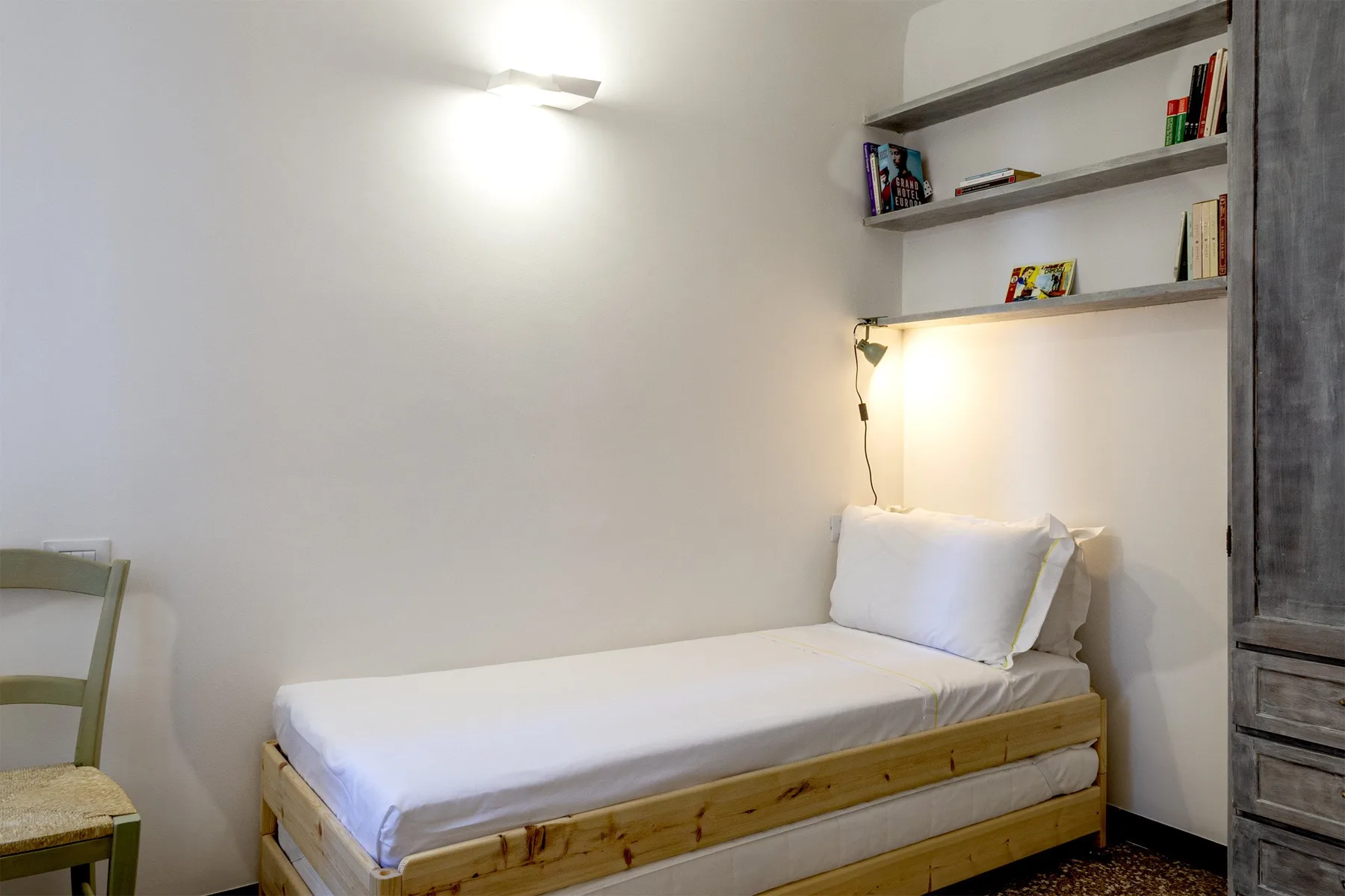 Una cama individual está bajo estantes de pared en un dormitorio sencillo.