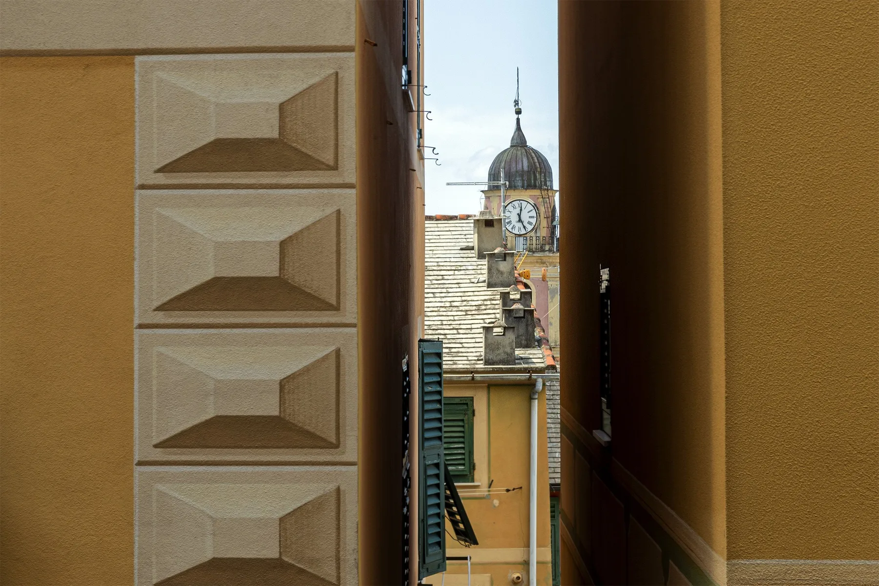A narrow view between buildings frames a domed clock tower above nearby rooftops.