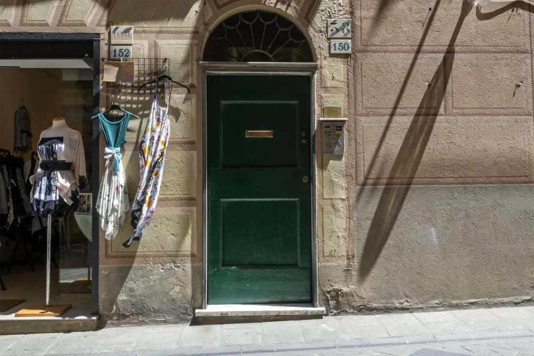 Una puerta de entrada verde oscuro está en una fachada de piedra junto al escaparate de una tienda.