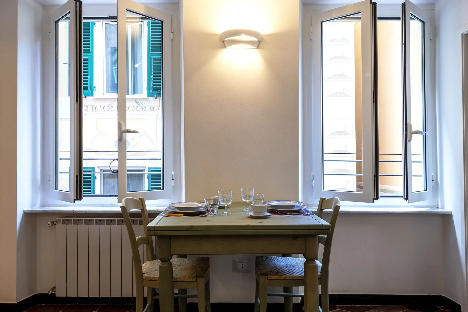 Un comedor con una mesa de madera entre dos ventanas abiertas.