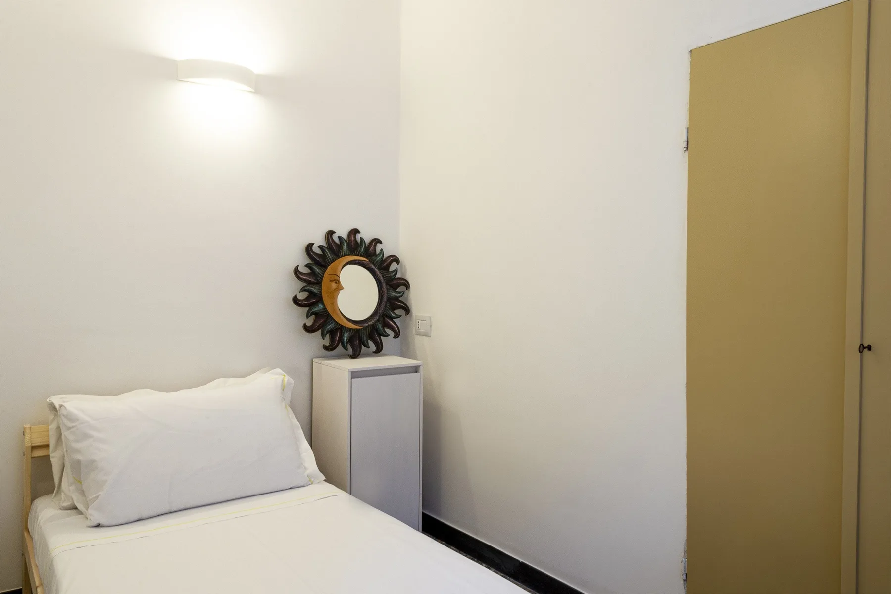 A bedroom with a bed, a small cabinet, and a wall mirror.