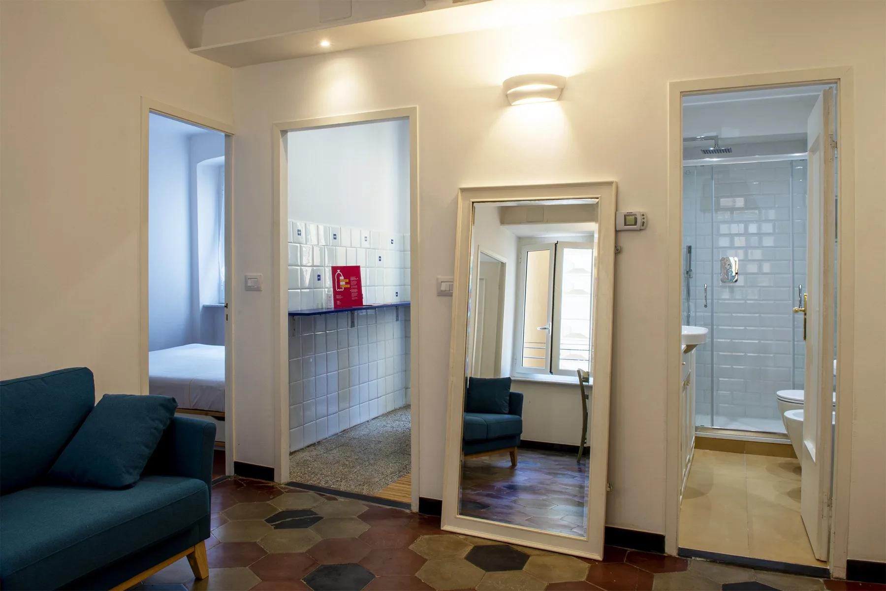 Una habitación con suelo de baldosas, un espejo alto y puertas a espacios contiguos.