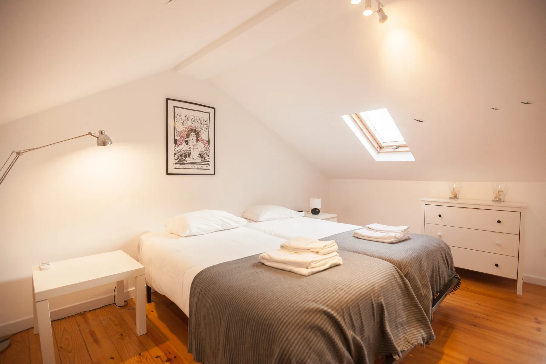 Un dormitorio con dos camas, una mesita de noche y techo inclinado.