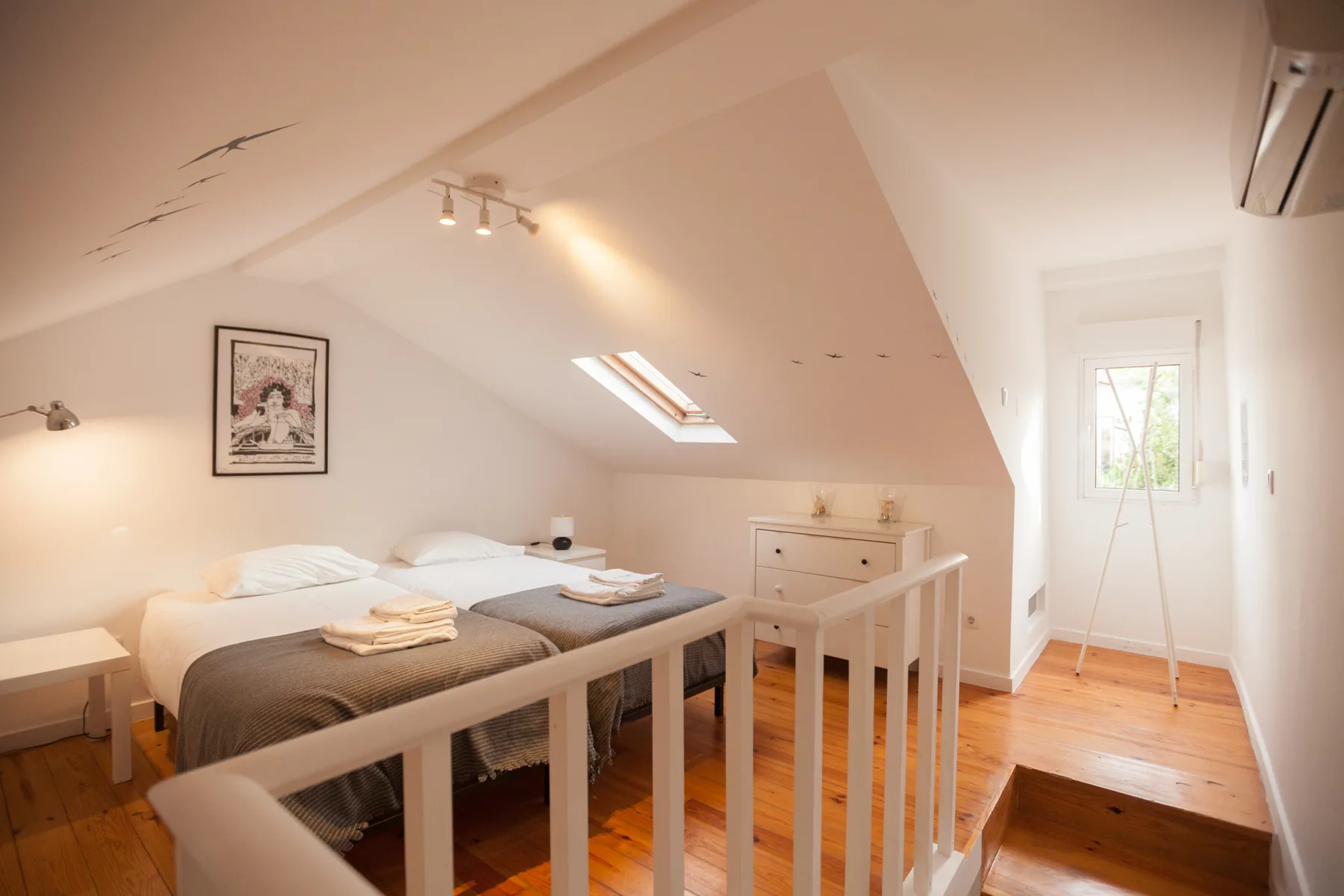 A bright attic bedroom with a bed beneath a sloped ceiling and a small skylight.