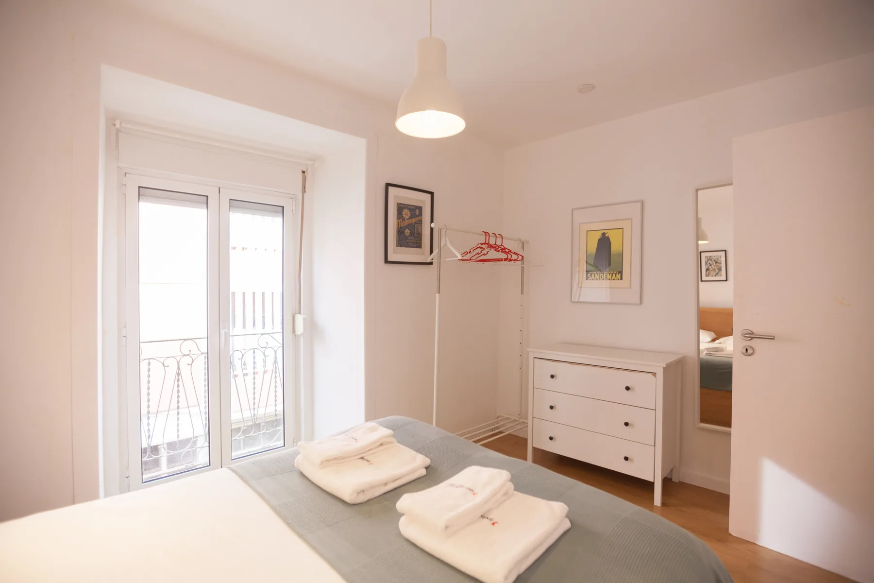 A bright bedroom with a bed, folded towels, a dresser, and a balcony door.