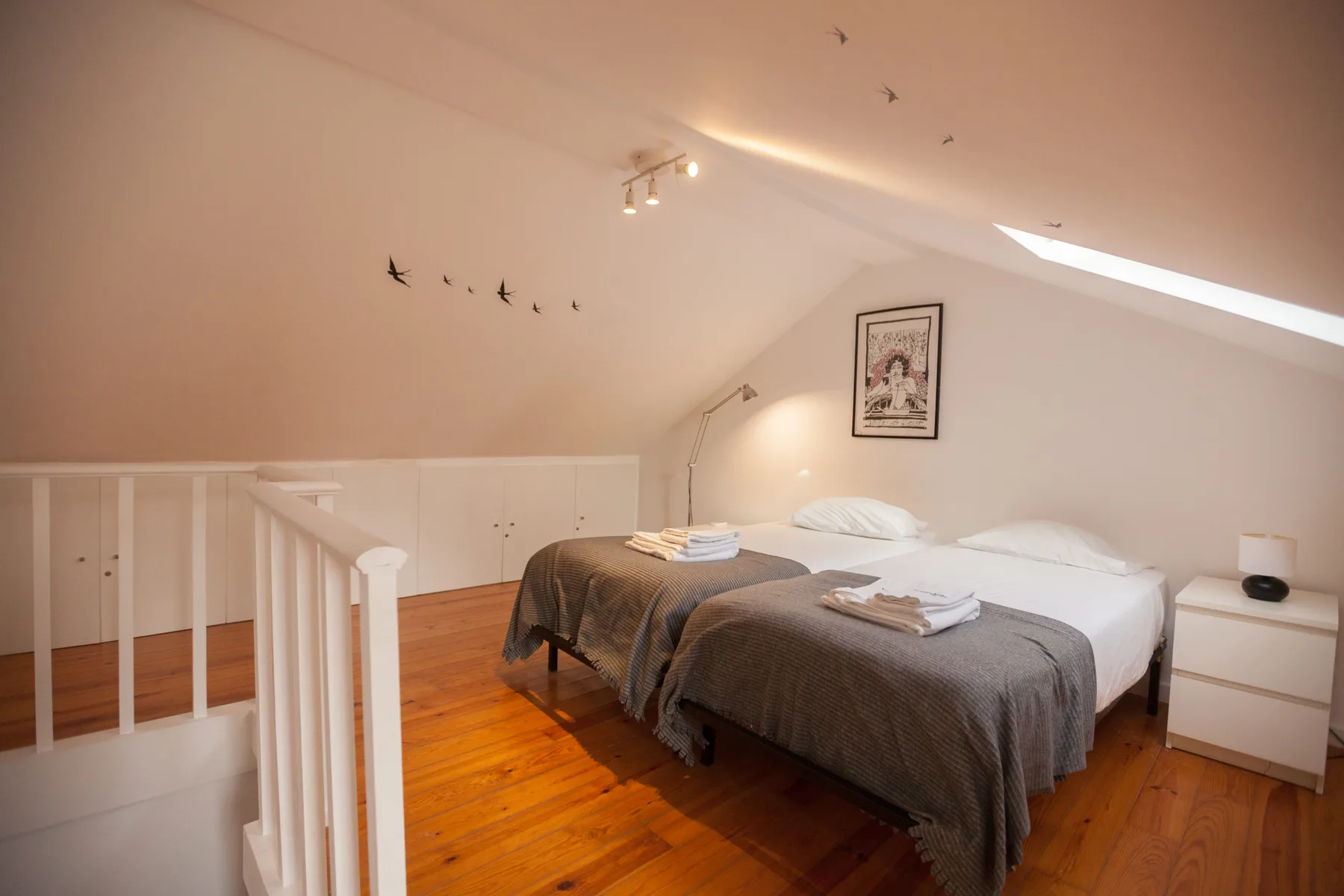 A bedroom with two beds, folded towels, and a sloped ceiling.