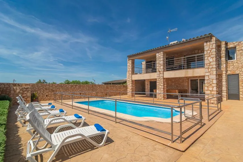A swimming pool and sun loungers sit beside a two-story stone-faced building.