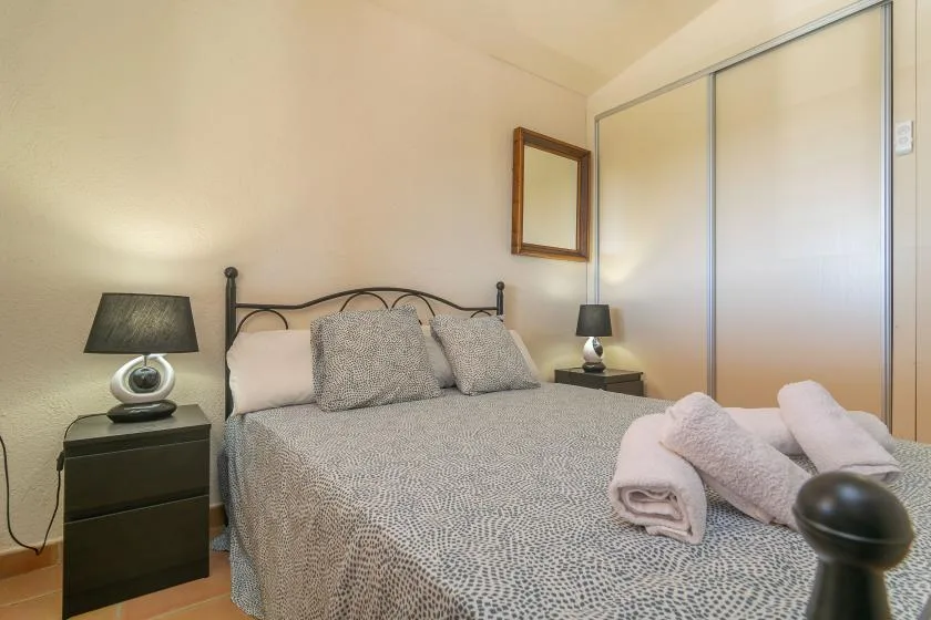 A bedroom with a neatly made bed and folded towels at the foot.
