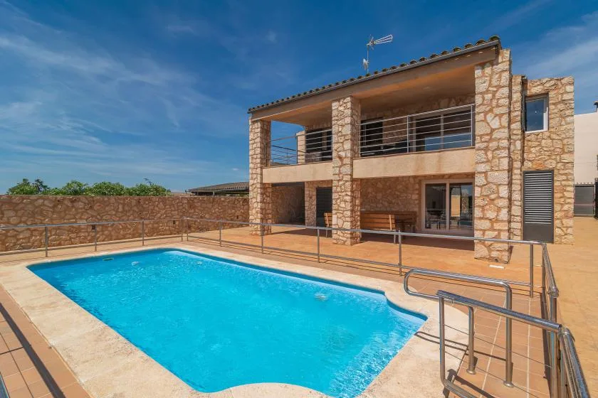 A stone house stands beside a swimming pool on a sunny terrace.