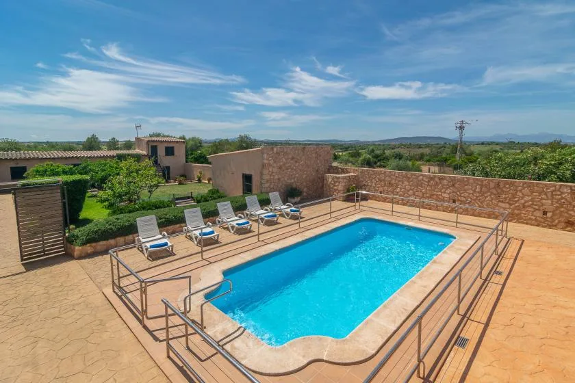 An outdoor swimming pool sits on a sunlit terrace beside a stone wall.