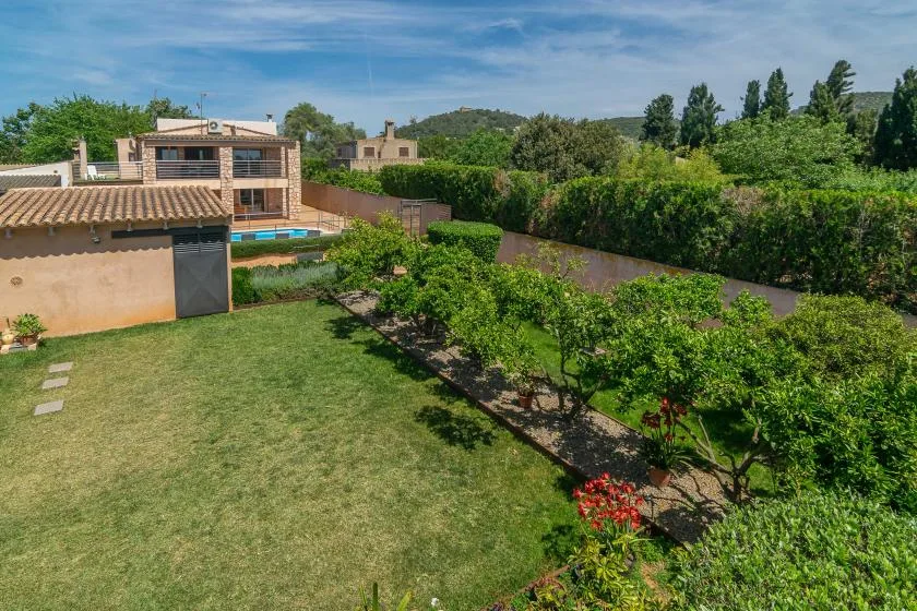 A landscaped garden with a lawn, flowering plants, and a swimming pool beside a house.