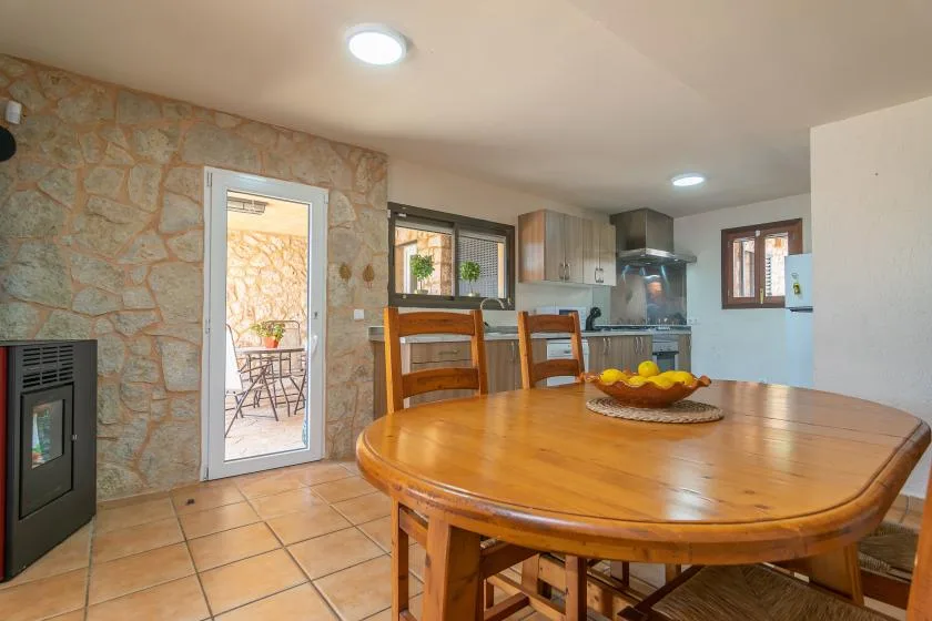 A dining area with a large wooden table beside a stone wall and kitchen.