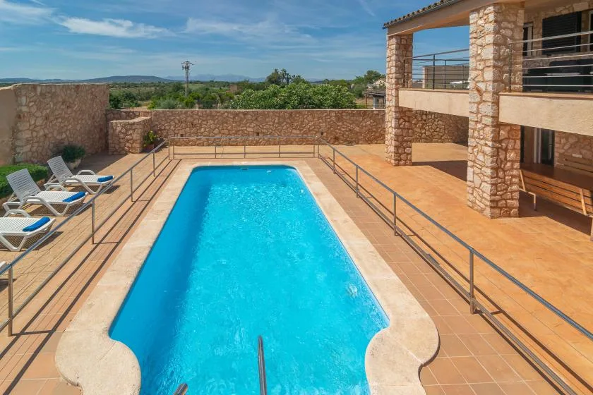 A swimming pool fills a sunlit terrace beside a stone building.