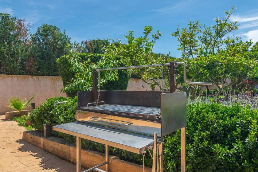 A metal grill stands beside a stone-paved patio surrounded by greenery.