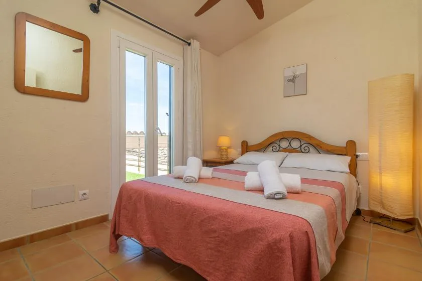 A bedroom with a double bed, folded towels, and glass doors opening to a balcony.
