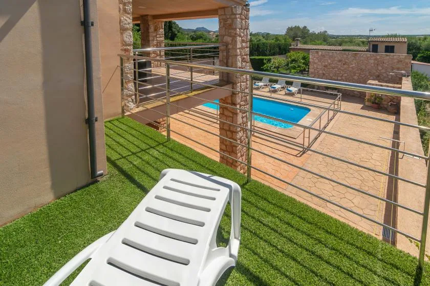 A sunlit outdoor pool area with a white lounge chair on a grassy terrace.