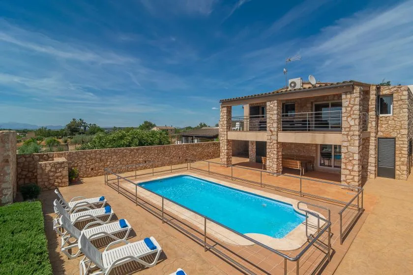 A swimming pool and lounge seating sit in front of a stone-clad building.