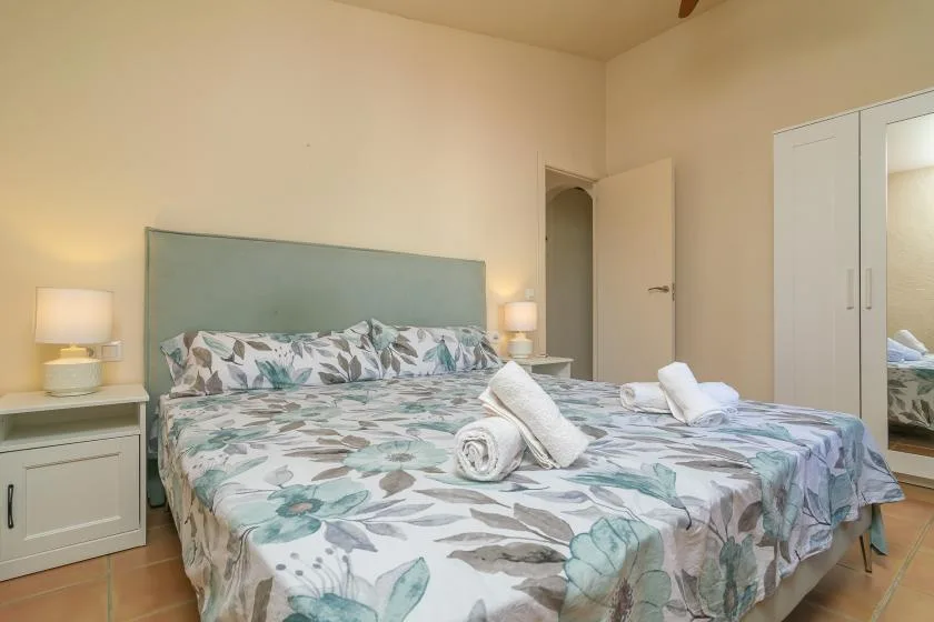 A bedroom with a large bed covered in blue-green floral bedding.
